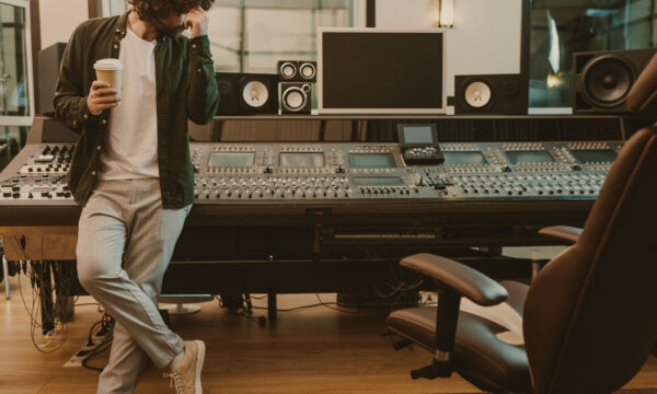 young sound producer standing at studio with cup of coffee to go